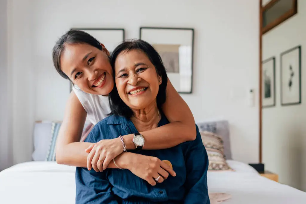 Daughter embracing mother from behind sitting in a white bedroom