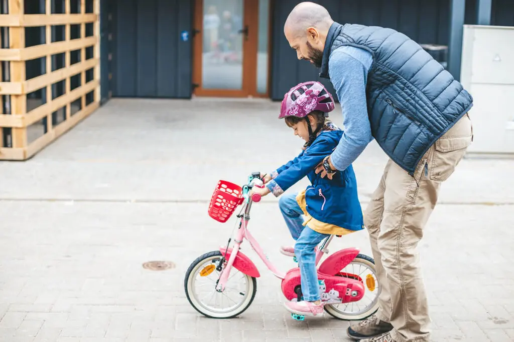 Father teaching his daughter how to ride a red training bicycle