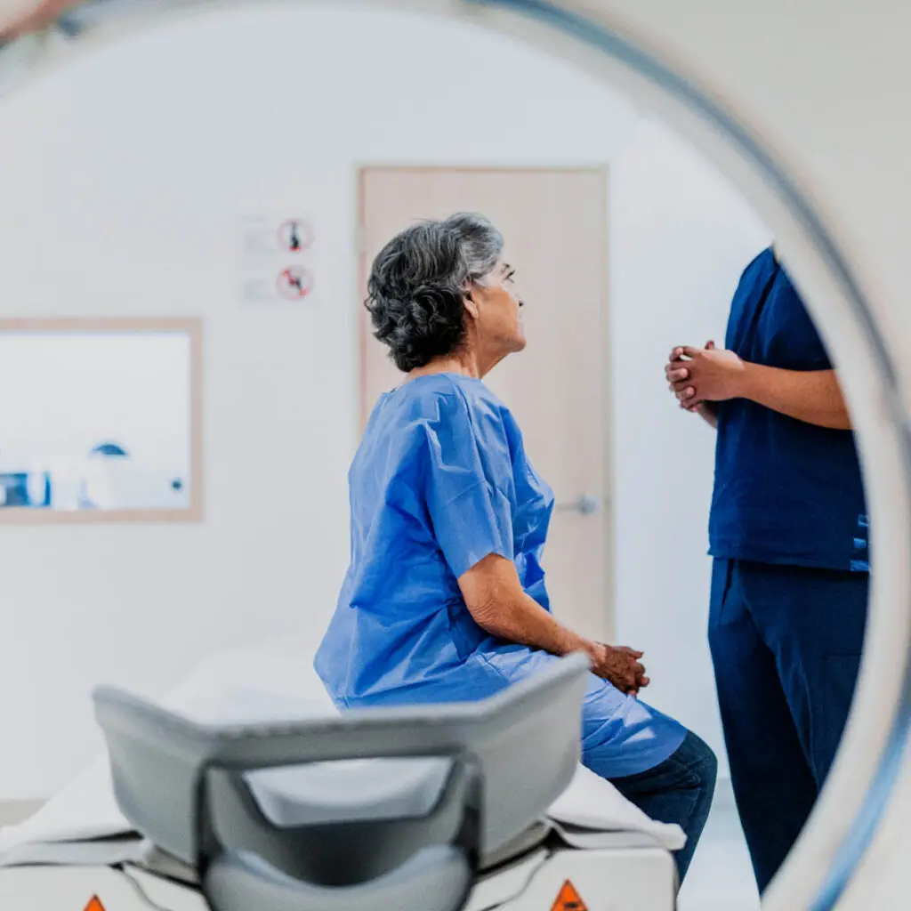 Patient sitting on bench of MRI machine, speaking with doctor