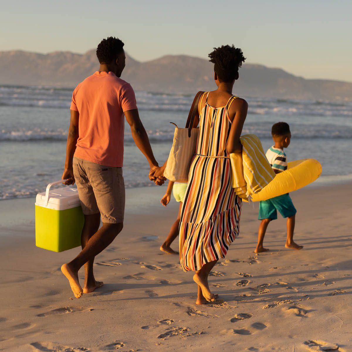 Family walking along the beach with toys and cooler in hand