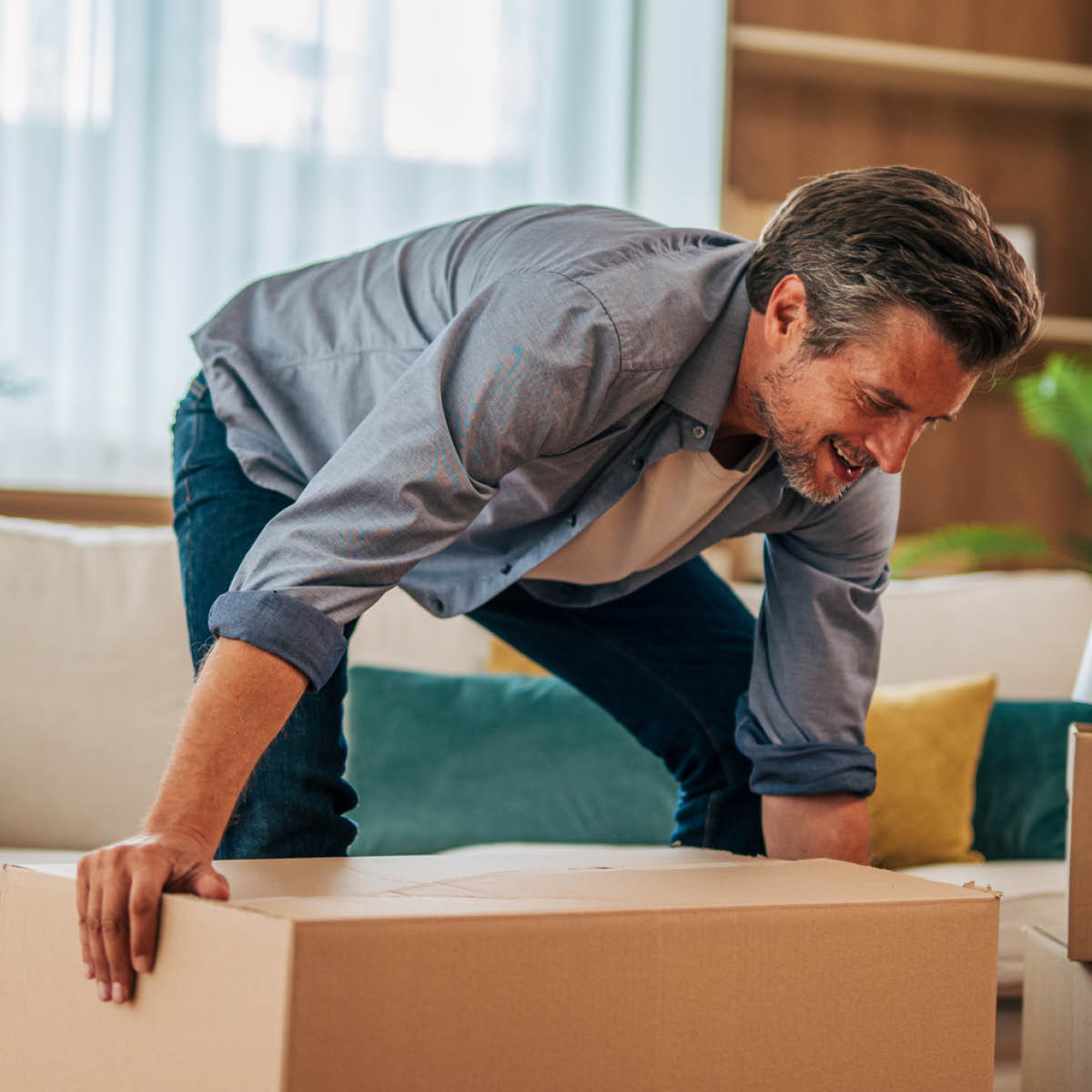 Middle aged man picking up a moving box in his living room