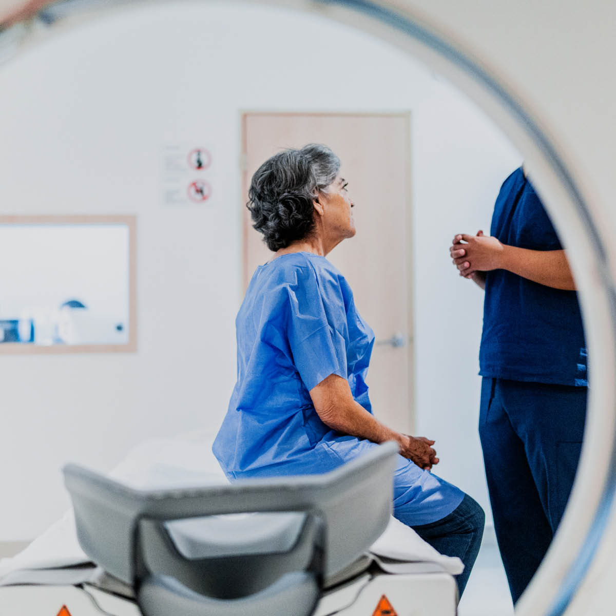 Patient sitting on bench of MRI machine, speaking with doctor